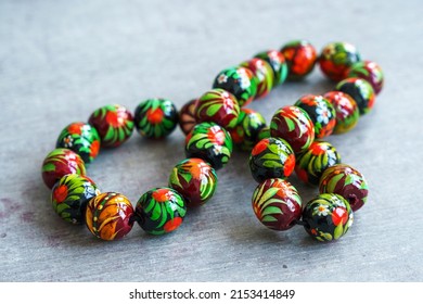 Wooden Beads In Slavic Folk Style On The Bright Wooden Table. Bead Necklace From The Carpathians. Slavic Folk Costume Necklace. Hand-painted With Flowers In The Ukrainian Style. Petrykiwka Painting.