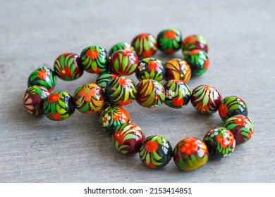 Wooden Beads In Slavic Folk Style On The Bright Wooden Table. Bead Necklace From The Carpathians. Slavic Folk Costume Necklace. Hand-painted With Flowers In The Ukrainian Style. Petrykiwka Painting.