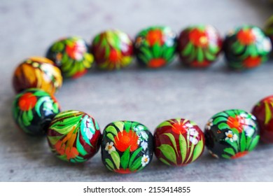 Wooden Beads In Slavic Folk Style On The Bright Wooden Table. Bead Necklace From The Carpathians. Slavic Folk Costume Necklace. Hand-painted With Flowers In The Ukrainian Style. Petrykiwka Painting.