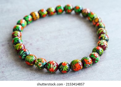 Wooden Beads In Slavic Folk Style On The Bright Wooden Table. Bead Necklace From The Carpathians. Slavic Folk Costume Necklace. Hand-painted With Flowers In The Ukrainian Style. Petrykiwka Painting.