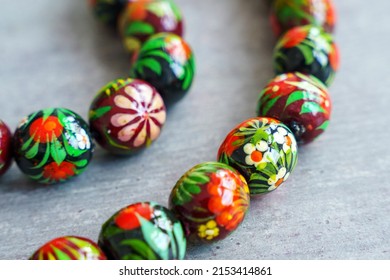 Wooden Beads In Slavic Folk Style On The Bright Wooden Table. Bead Necklace From The Carpathians. Slavic Folk Costume Necklace. Hand-painted With Flowers In The Ukrainian Style. Petrykiwka Painting.