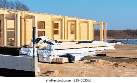 Wooden beams lie wrapped in plastic at the construction site of a modern wooden house. Storage of building materials on the building sand at the construction site. 