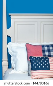 Wooden Bed Painted White Against A Blue Wall. Pillows In A Red, White And Blue Color Theme.