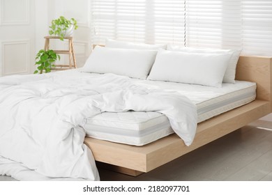 Wooden bed with soft white mattress, blanket and pillows in cozy room interior