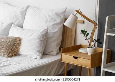 Wooden bedside table with lamp and flowerpot in light room