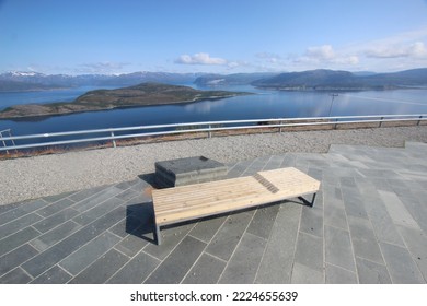 A wooden bench bed at a reststop in the north of norway. Looking out over the sea and some small islands. The sun is shining.