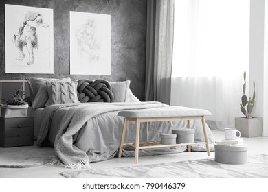 Wooden Bench And Boxes In Monochromatic Bedroom Interior With Drawings On Concrete Wall Above Bed