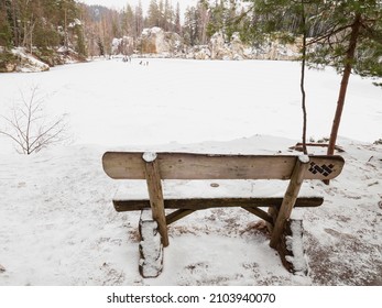 Wooden bench by the frozen blue lake. Winter tracking in popular in Adrspach rocky labyrinth in Czech Republic.