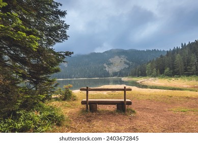 Wooden bench by walking path in coniferous forest near Black Lake in Durmitor National Park, Montenegro. Morning scenic landscape with bench for tourists rest with panorama of misty Crno Jezero. - Powered by Shutterstock