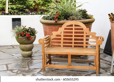 A Wooden Bench With A Large Plant Pot Behind It