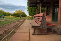 A Wooden Bench In An Old Abandoned Train Station With A View Of The Railroad With Grass Around It
