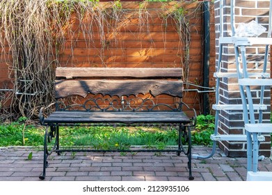 wooden bench on a metal forged base stands in front of the house. place to rest near the wall.