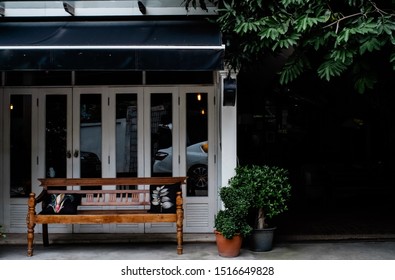 Wooden Bench With Pillows And Pot Of Plants In Front Of White And Glass Folding Doors House.