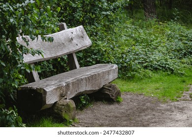 A wooden bench is sitting in a grassy area with trees in the background. The bench is old and has a rustic appearance. The scene is peaceful and serene - Powered by Shutterstock