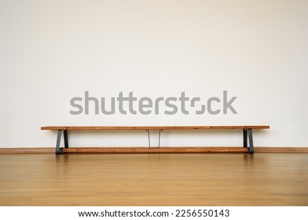 Wooden bench standing on floor in empty sport gymnasium hall. School gym with bench against white blank wall.
