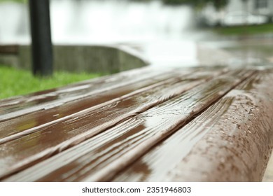 Wooden bench with water drops outdoors, closeup. Rainy weather