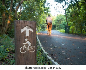 Wooden Bicycle Sign Beside The Road In Park With Blurry Riding M