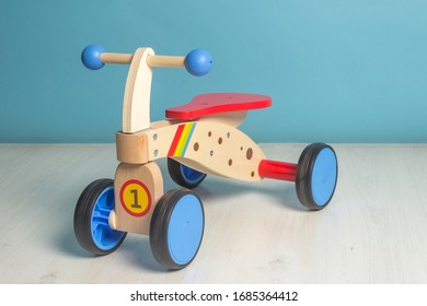 Wooden Bicycle Toy For Kids To Learn To Drive.
Push Bike In A Room In Wooden Floor And Blue  Background.