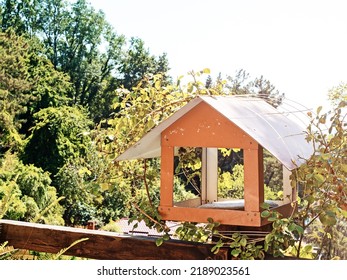 Wooden Bird Feeder On The Fence. A Bird Feeder Made Of Plywood On A Wooden Fence In The Yard On A Sunny Summer Day. Focus On Bird House