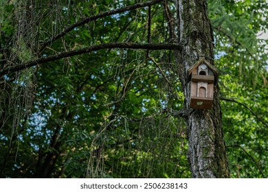 A wooden birdhouse attached to a tree with lush greenery in the background. - Powered by Shutterstock