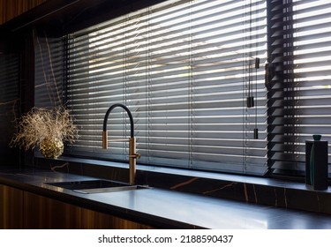 Wooden blinds black color closeup on the window. Bamboo slats 50mm wide. Venetian wood blinds in the kitchen. Black tapes. Sink with copper faucet near the window. Round vase is on the windowsill. - Shutterstock ID 2188590437