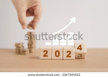 wooden block cube  with 2024, last one flipped 3 to 4 and increasing graph with blurred hand arranged coins stacking for setup objective target business cost and budget planing of new year concept
