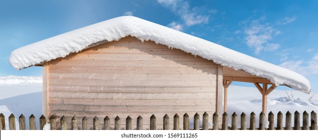 Blockhaus aus Holz mit schneebedecktem Dach und Gitterzaun am blauen Himmel. Winterhintergrund.