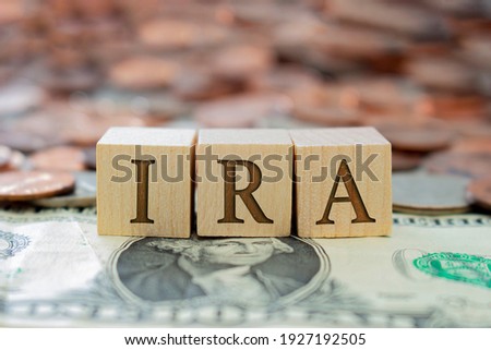 Wooden block with the letter IRA with some money around. Concept: Retirement Plan in USA, Individual Retirement Account