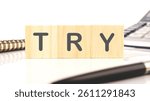 Wooden blocks display the word try, positioned alongside a spiral notebook and a black pen on a minimalistic desk in a contemporary office environment.