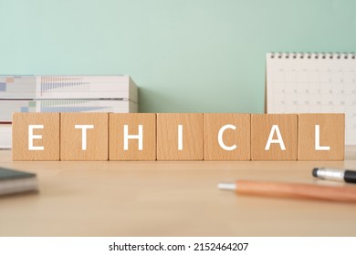 Wooden blocks with "ETHICAL" text of concept, pens, notebooks, and books.