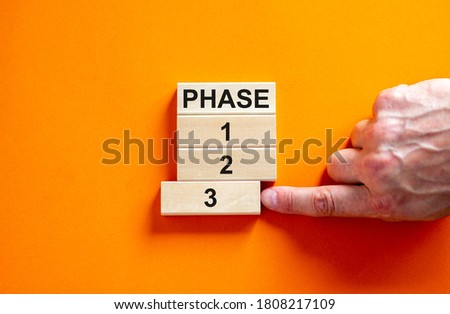 Wooden blocks form the words 'phase, 1, 2, 3,' on orange background. Male hand. Beautiful background. Business concept.