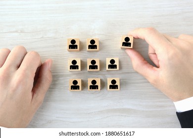 Wooden blocks with human pictogram picked out from employee group by business man's hand
