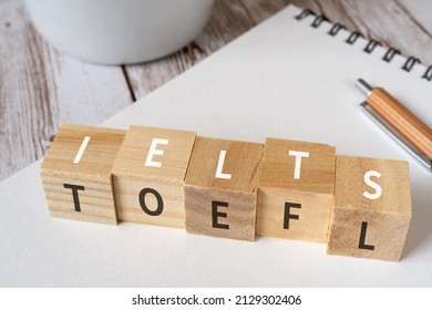 Wooden blocks with "IELTS" and "TOEFL" text of concept, a pen, a notebook, and a cup. - Shutterstock ID 2129302406