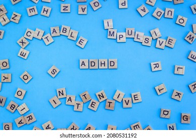 Wooden Blocks With Letters ADHD And Chaotic Words On A Blue Background. Minimal Concept Of Attention Deficit Hyperactivity Syndrome. Selective Focus