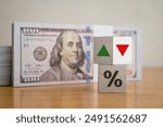 Wooden blocks percentage sign, arrow up and down with heap US dollar banknotes background. Central bank FED (Federal Reserve System) control interest rate increase or decrease. Global economy concept.