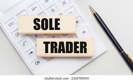 Wooden blocks with the SOLE TRADER Iie on a light background on a white calculator. Nearby is a black handle. Business concept