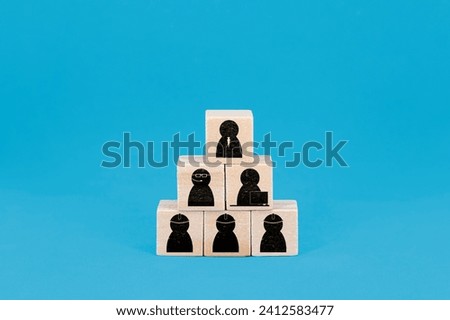 Wooden blocks stacked in a pyramid shape, each featuring an icon representing different roles in a corporate hierarchy, against a blue background with copy space.