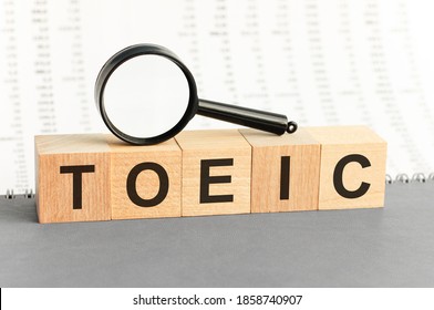 Wooden Blocks with the text: TOEIC with magnifying glass. TOEIC word made with building blocks. Business concept