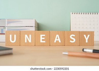 Wooden blocks with "UNEASY" text of concept, pens, notebooks, and books. - Shutterstock ID 2230592201