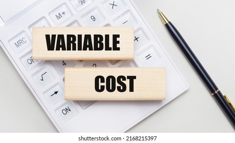 Wooden Blocks With The VARIABLE COST Iie On A Light Background On A White Calculator. Nearby Is A Black Handle. Business Concept