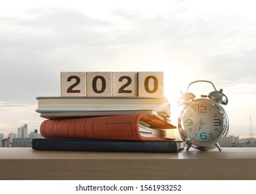 Wooden Blocks With The Word 2020, Notebook, Books And Clock On Table With Panoramic City Skyline Background In The Morning. Happy New Year, Start Up, Refresh, Mindset Concept.