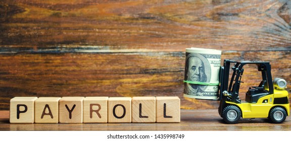 Wooden Blocks With The Word Payroll, Money And A Forklift. Payroll Is The Sum Total Of All Compensation A Business Must Pay To Its Employees For A Set Period Of Time Or On A Given Date. Taxes.