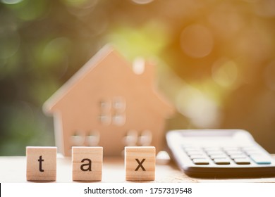 Wooden Blocks With The Word TAX With Blurred Calculator, Wooden House Toys With Blurred Green Background - Tax Concept.