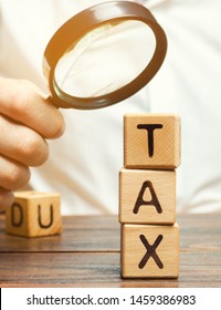 Wooden blocks with the word Tax and a magnifying glass in the hands of a businessman. The concept of studying the size of taxes. Taxation. Time to pay taxes. Tax on personal income. Agent. Taxpayer