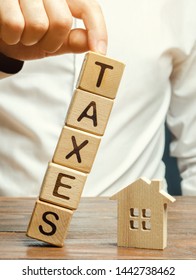 Wooden Blocks With The Word Taxes Fall On A Miniature House. The Concept Of The Tax Burden On Housing, Apartment, Property. Mortgage. Taxation. Taxpayer. Commercial Real Estate. Soft Selective Focus