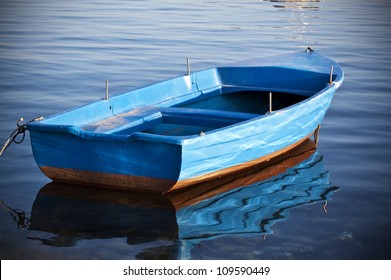 Wooden blue and empty boat of a fisherman in a still and calm water - Powered by Shutterstock