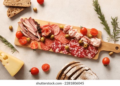 Wooden board with assortment of tasty deli meats and bread on light background