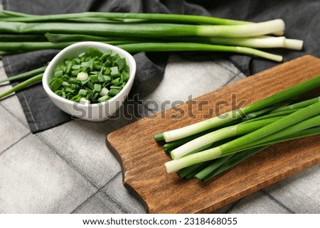 Wooden board and bowl with fresh green onion on dark tile background