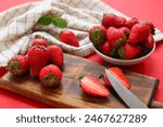 Wooden board and bowl with sweet fresh strawberries on red background