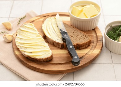 Wooden board with bread slices, garlic and bowl of fresh butter on white tile background - Powered by Shutterstock